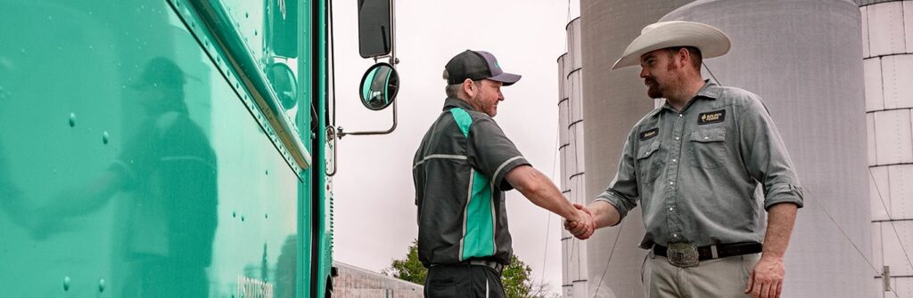 A UniFirst Route Service Representative (RSR) greets his customer during one of his regularly scheduled uniform and product pickup and delivery services that is part of a UniFirst managed uniform rental program. This customer is wearing a Dickies® Canvas Work Shirt and SofTwill® Flat Front Flexwaist Pants (pants are exclusively manufactured by UniFirst).