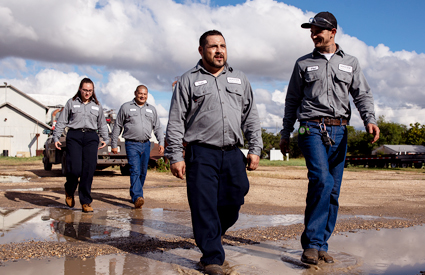 Four uniformed workers walking through a dirt area wearing UniFirst uniforms