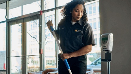Woman in UniFirst grey polo shirt, looking down and using mop to clean floor