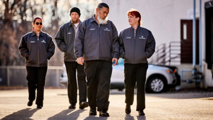 Group of workers wearing UniFirst work pants walking in a parking lot.