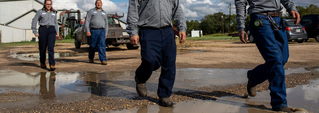 Industrial workers in flame resistant safety work pants walking in a work zone.