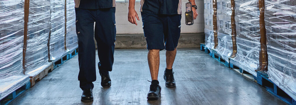 Industrial wholesale workers walking in a warehouse wearing UniFirst enhanced visibility pants.