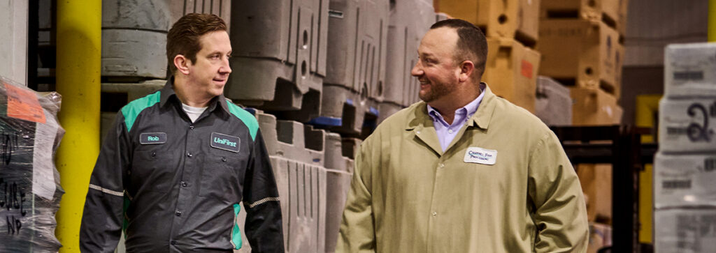 A UniFirst RSR walking and discussing work uniform rental service with his customer in a warehouse setting