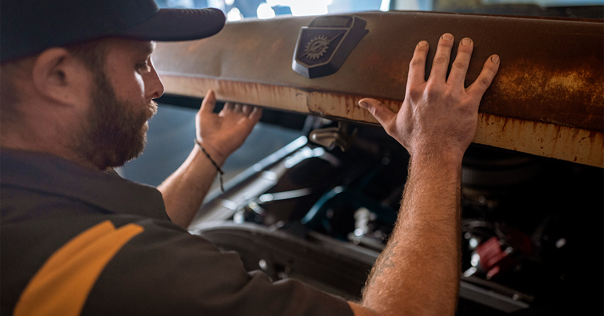 Automotive worker wearing a UniFirst uniform shirt closing the hood of a car being worked on