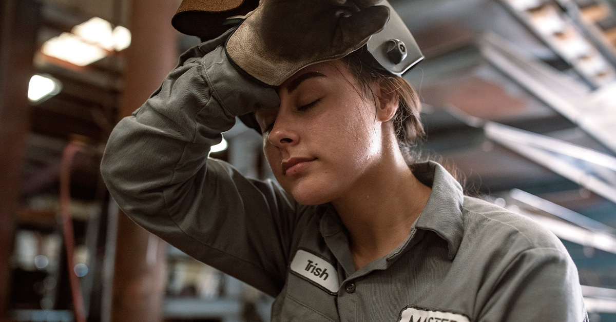 A woman working in contracting and trades wipes her forehead while wearing a UniFirst FR uniform