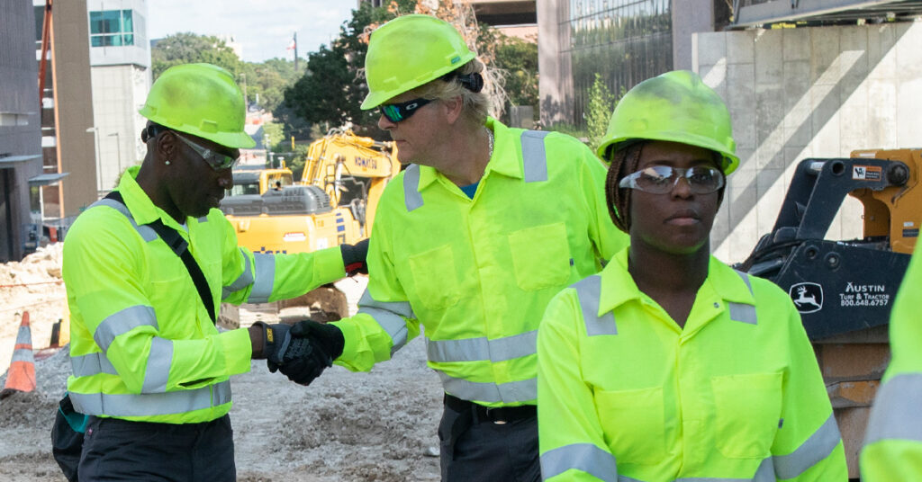 A group of construction workers wearing UniFirst high-visibility garments shaking hands on a job site