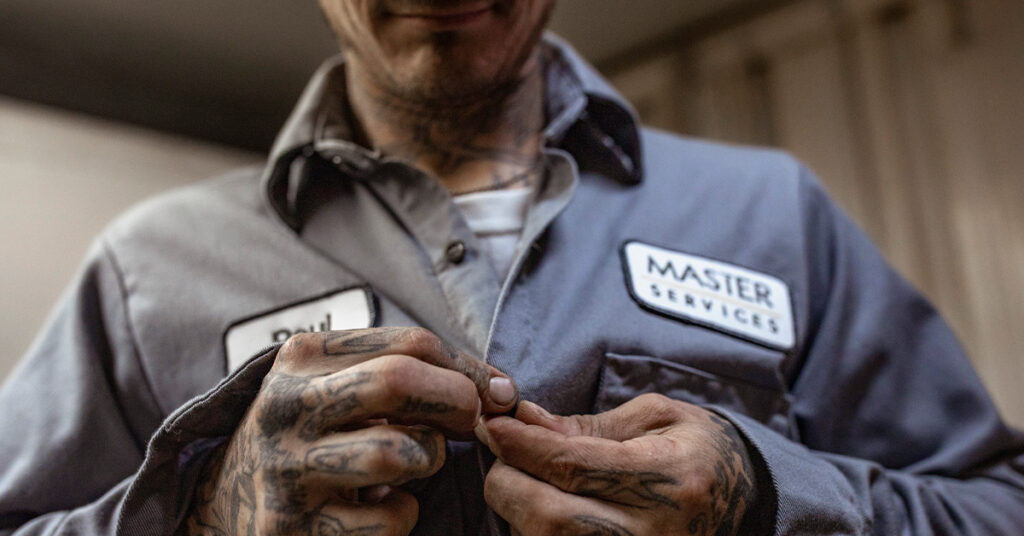 A closeup of a man buttoning his UniFirst uniform shirt with a focus on the shirt's emblems.