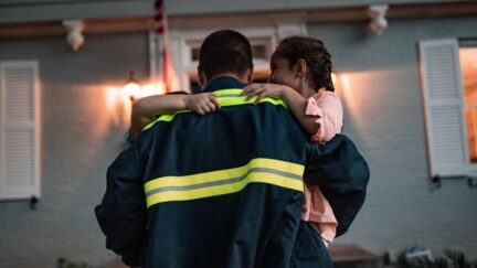 A man carrying his two children after coming home from work wearing a industrial laundered uniform from UniFirst