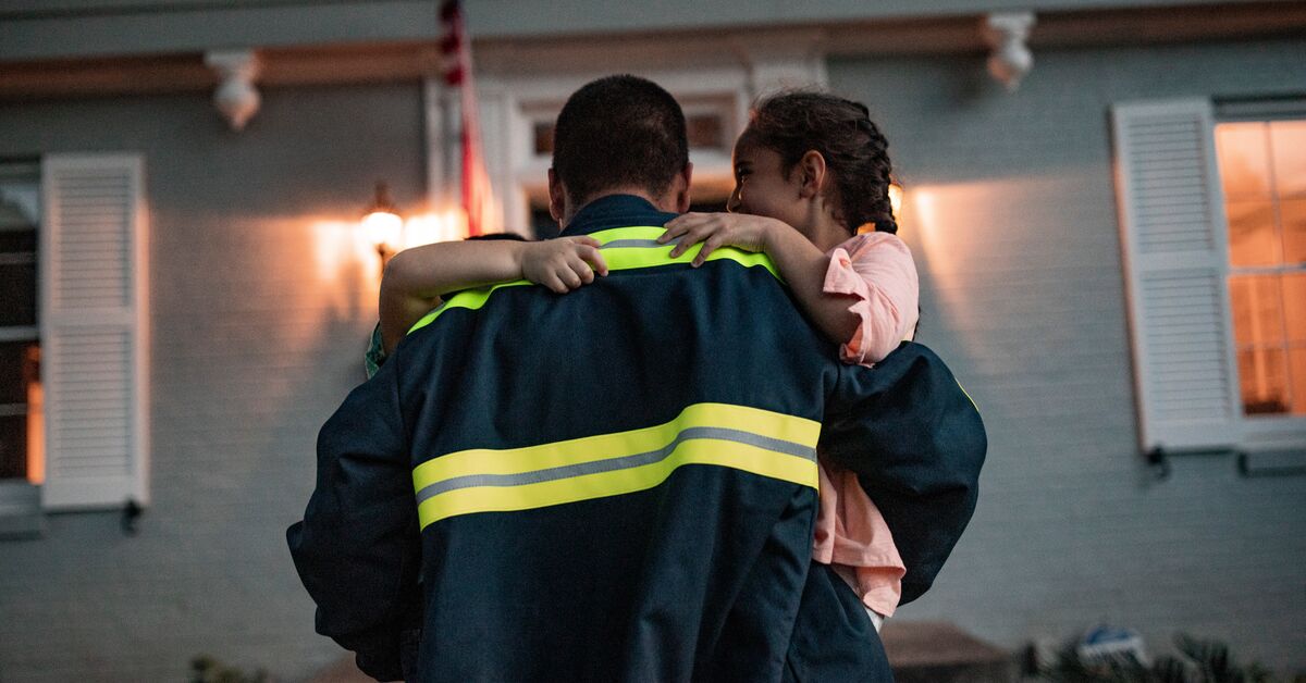 A man carrying his two children after coming home from work wearing a industrial laundered uniform from UniFirst