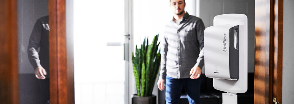 Industrial hygiene in the workplace with a man walking towards a hand sanitizer dispenser