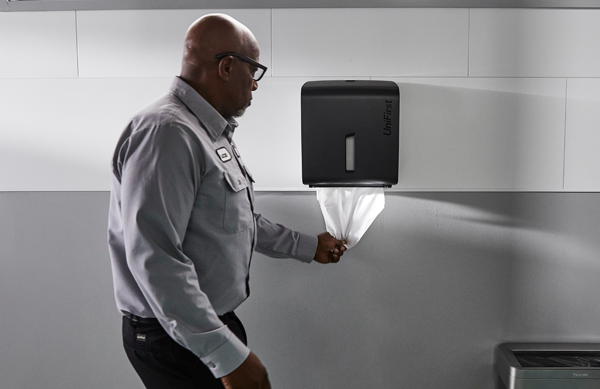 A man using an Essential Series Paper Towel Roll Dispenser in a commercial restroom