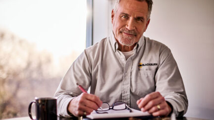 A man sitting at a table smiling while wearing a UniFirst uniform knowing his procurement strategy is in control.