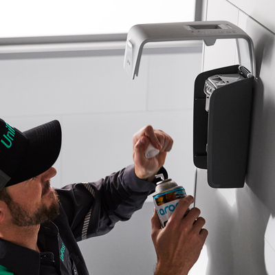 A UniFirst RSR replacing an empty automatic air freshener dispenser with a new refill
